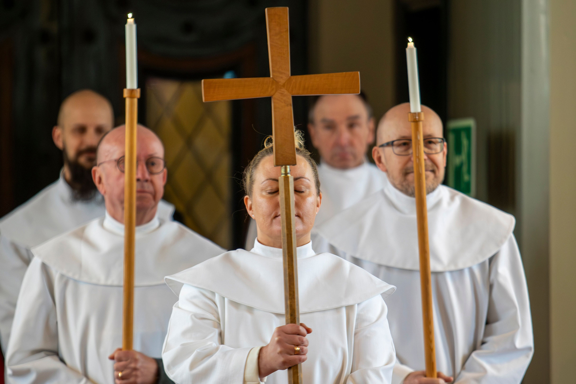 Fyra män och en kvinna i vita kåpor bär kors och ljus.