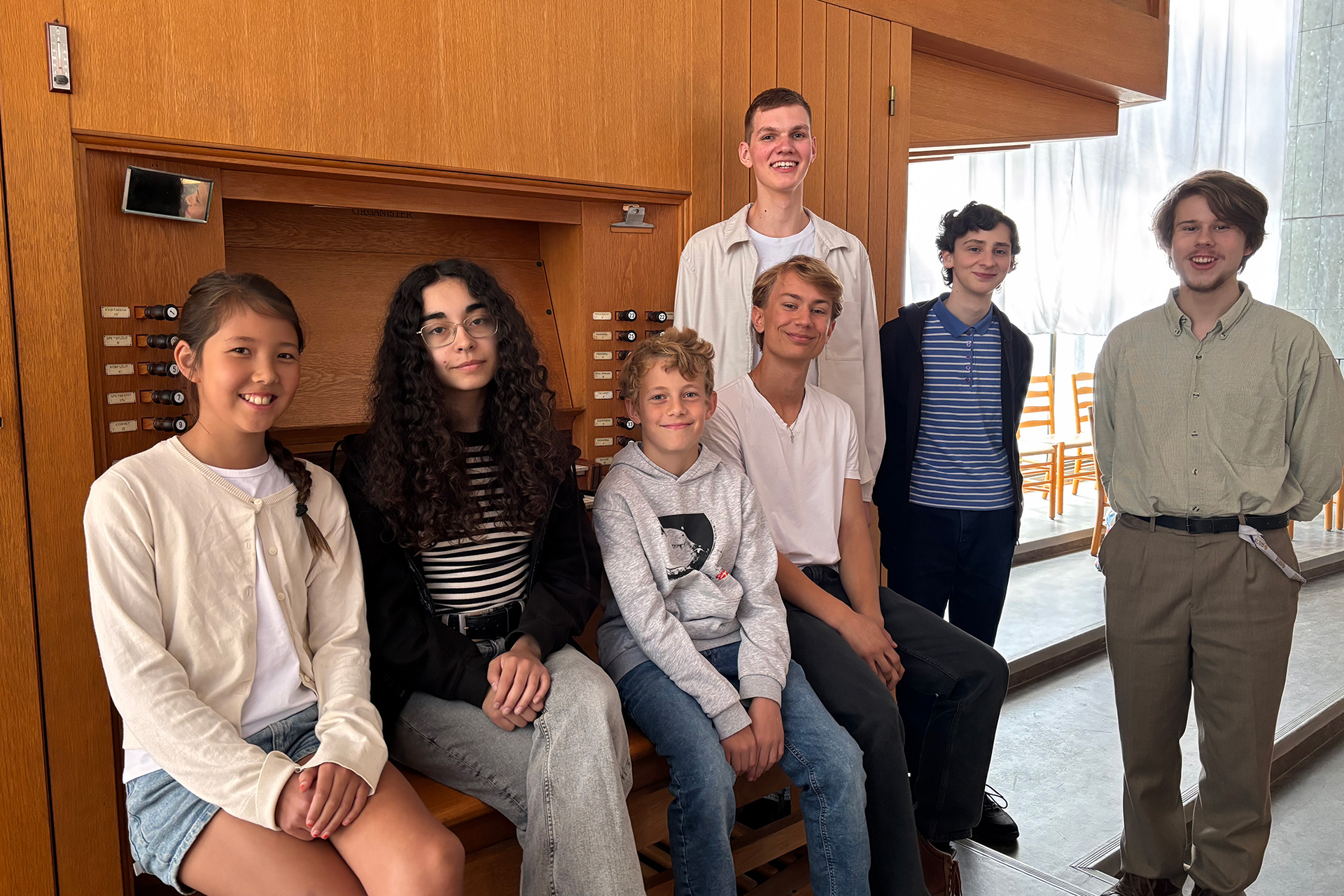 Fem killar och två tjejer sitter och står framför läktarorgeln i S:t Andreas kyrka.