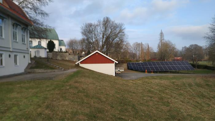 Solcellsanläggning stående på marken mellan kyrkan och församlingshuset.