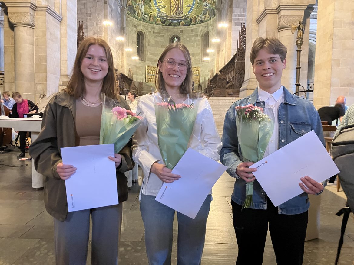 Två tjejer och en kille håller i varsitt papper och blombukett.