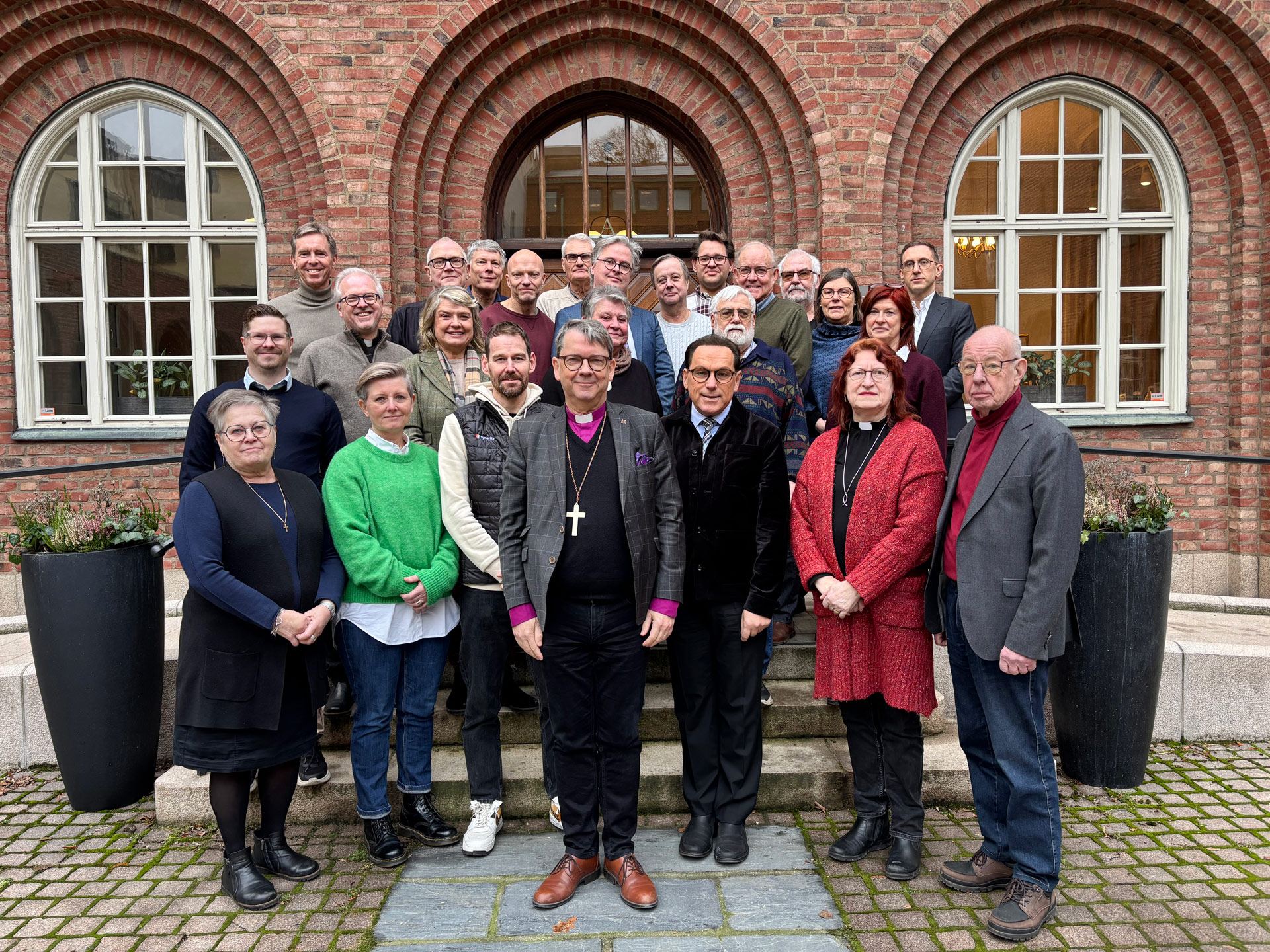 Människor står på en trappa framför ett tegelhus med fönster. 