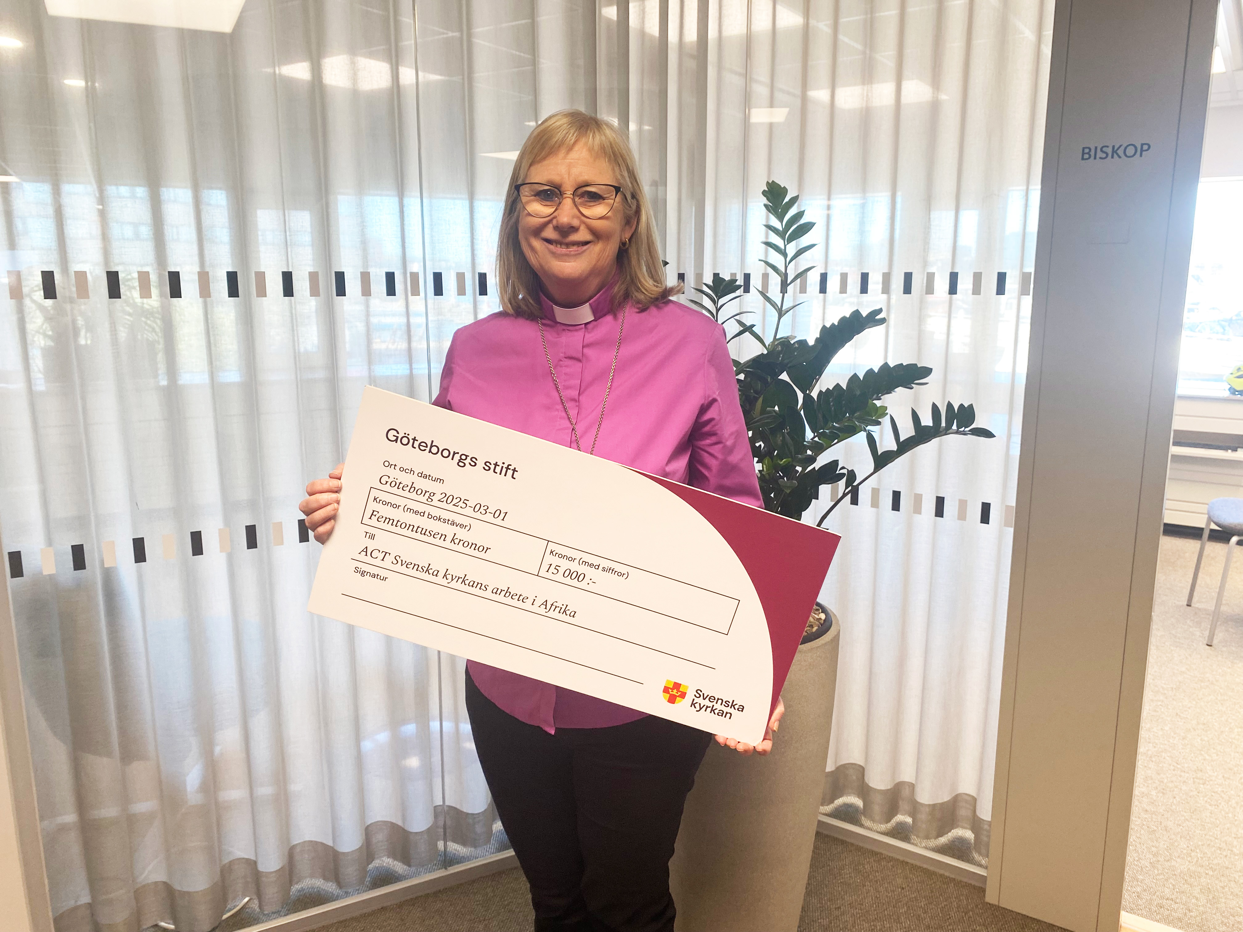 Biskop Susanne tar emot en check från stiftsstyrelsen på 15 000 kronor.