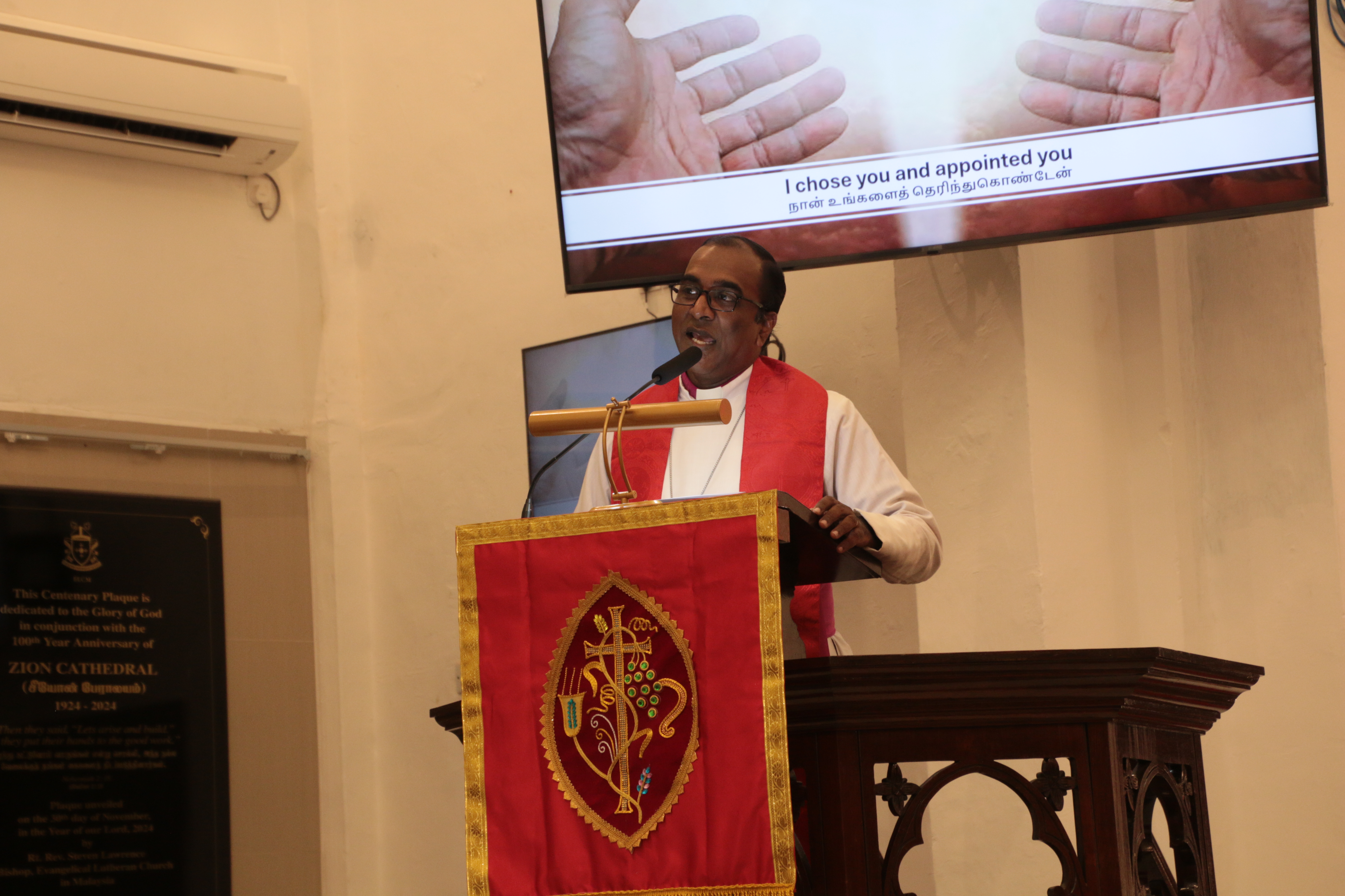 En man står vid en predikstol och talar engagerat.