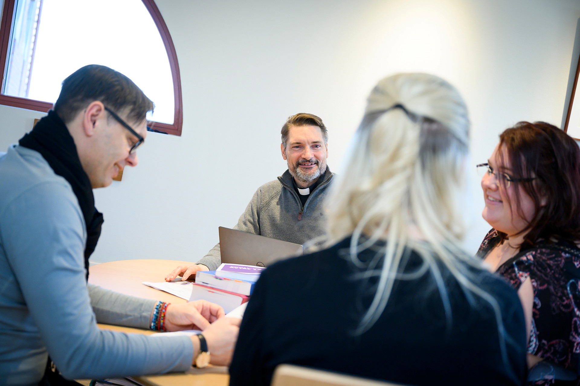 En grupp vuxna, varav en i prästskjorta, sitter och diskuterar runt ett bord.