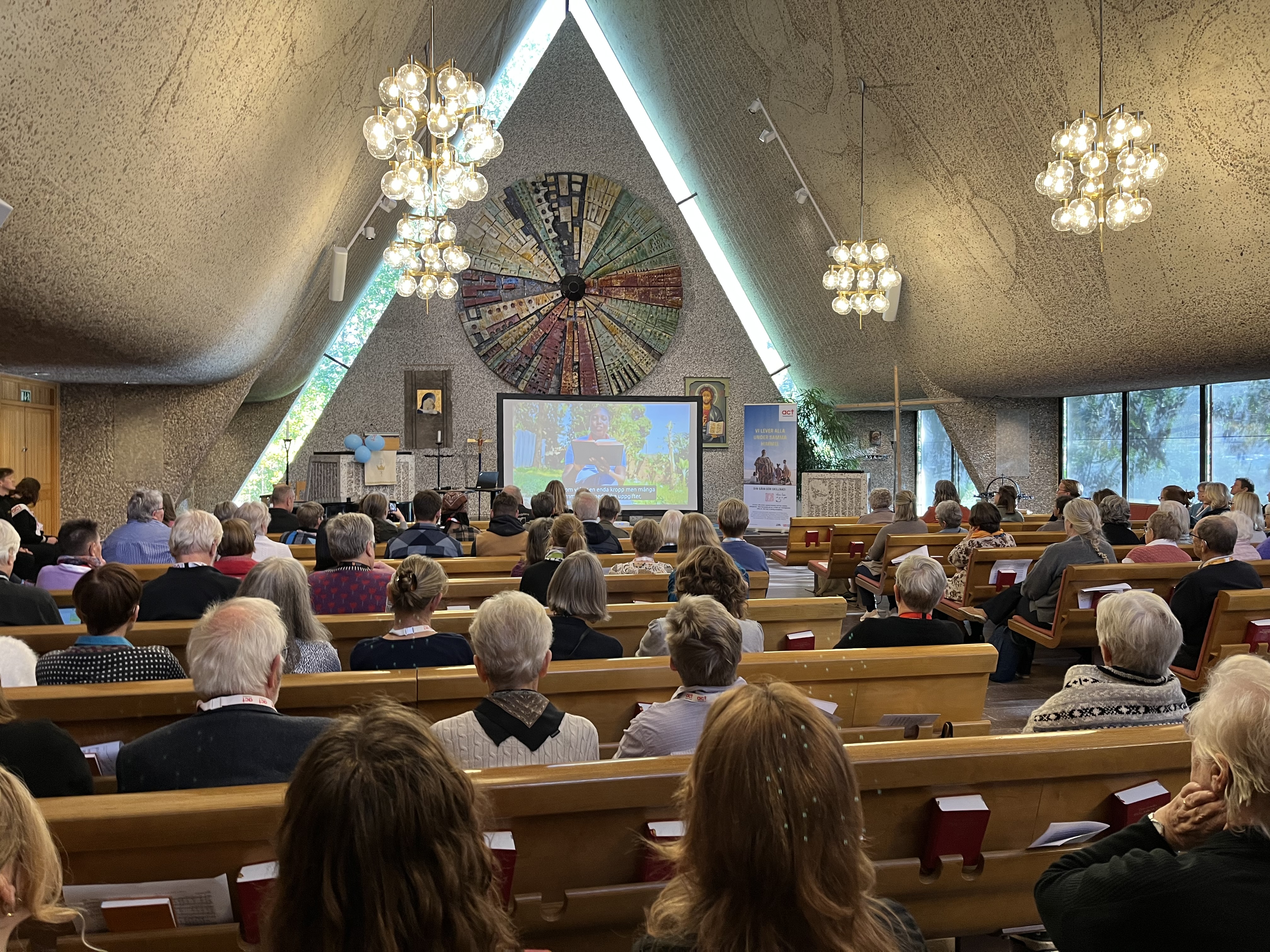 En kyrka full med människor som tittar fram mot altaret, där en film visas på en stor duk..