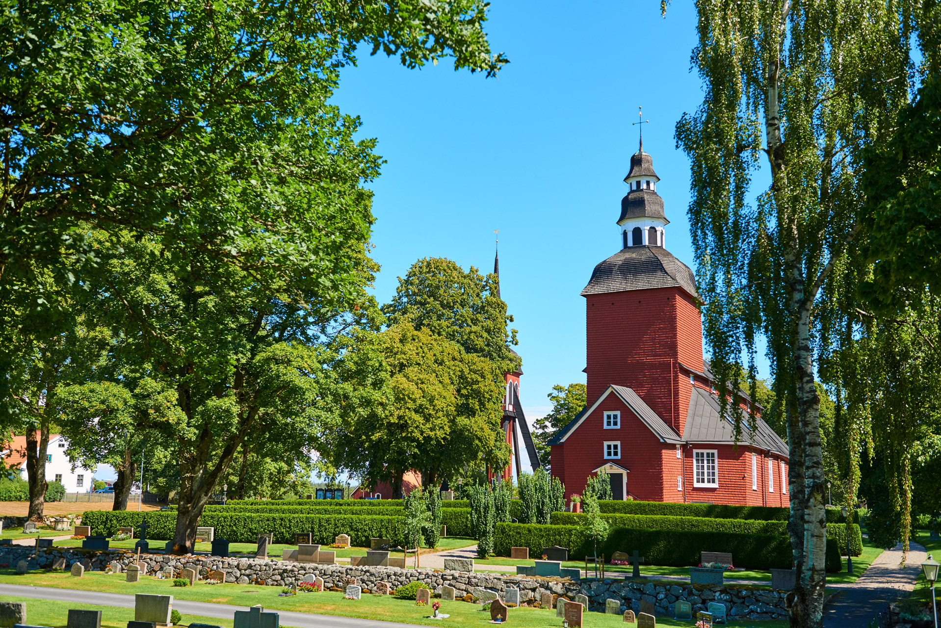 Röd träkyrka i grön lummig omgivning. Habo kyrka.