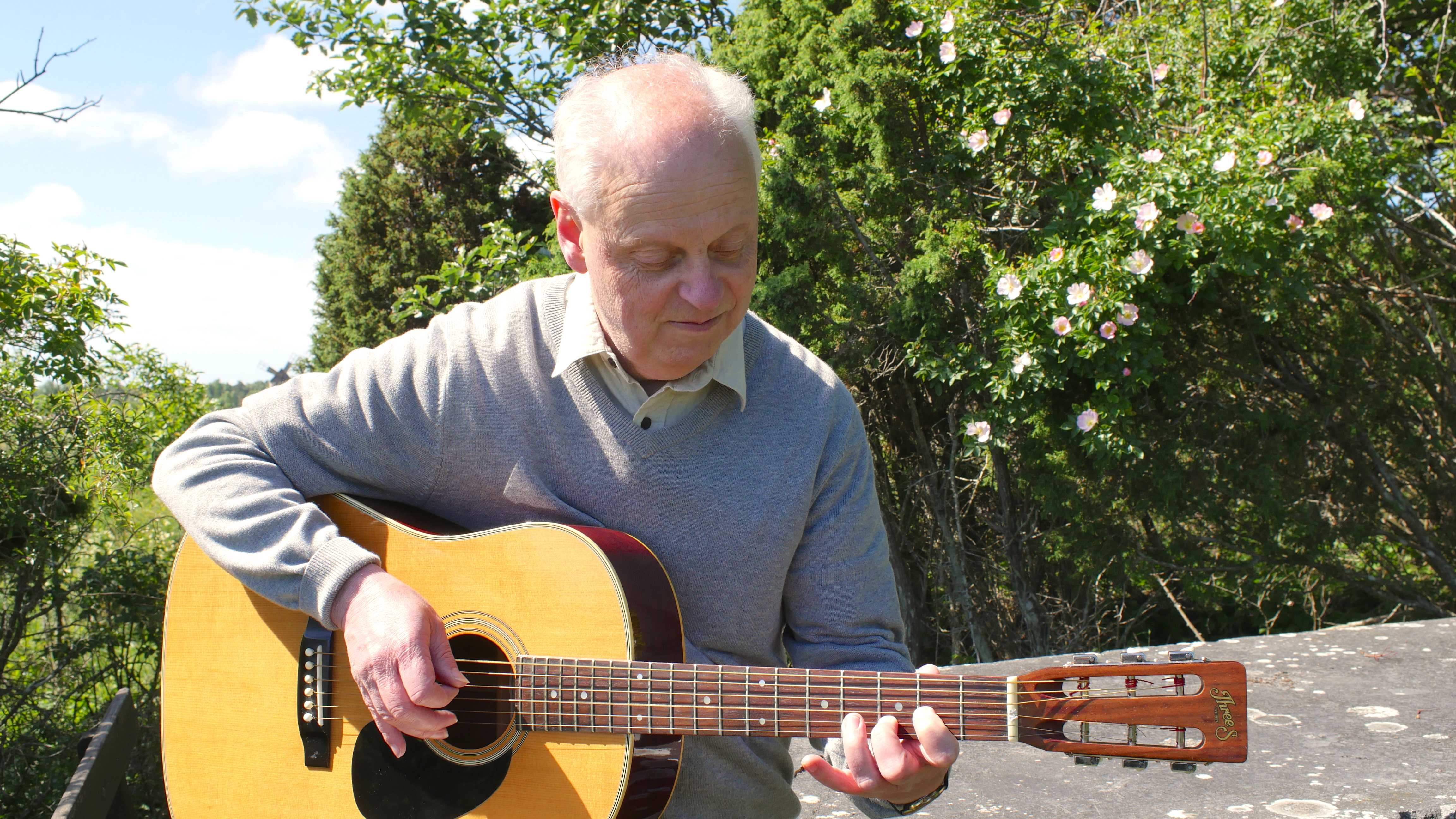 Jan Ekedahl sitter och spelar gitarr utomhus