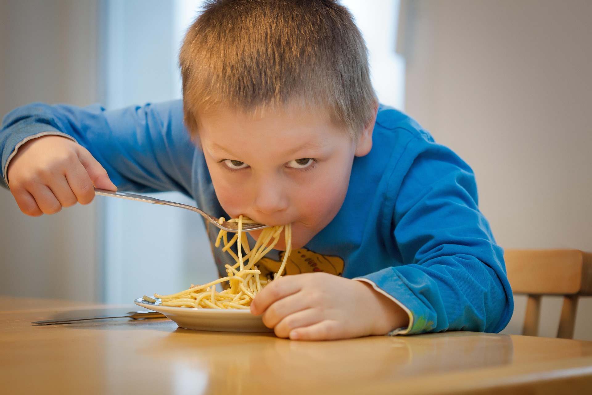 Pojke med munnen full av pasta och en intensiv blick