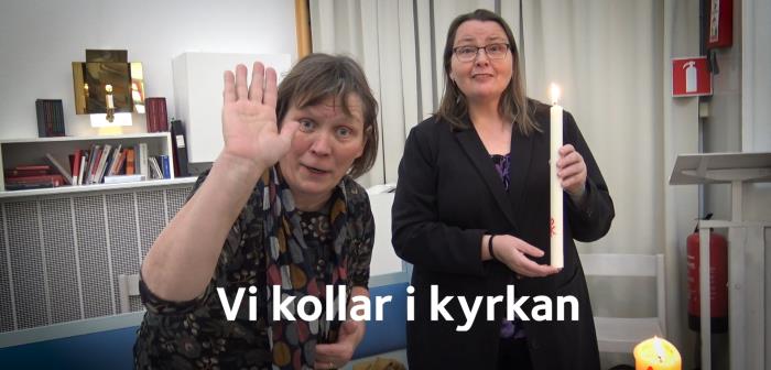 Två kvinnor står i en kyrkolokal. Den ena vinkar och den andra håller ett tänt stearinljus.