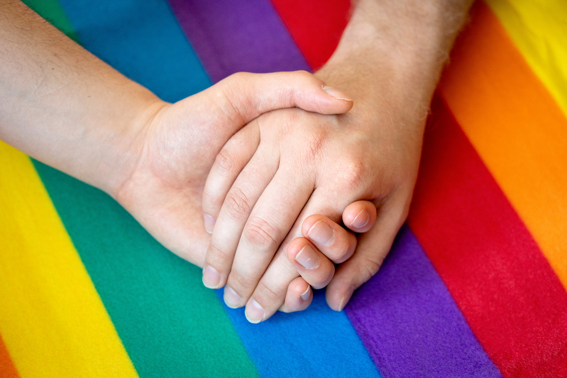Händer som håller varandra med regnbågsflaggan i bakgrunden.