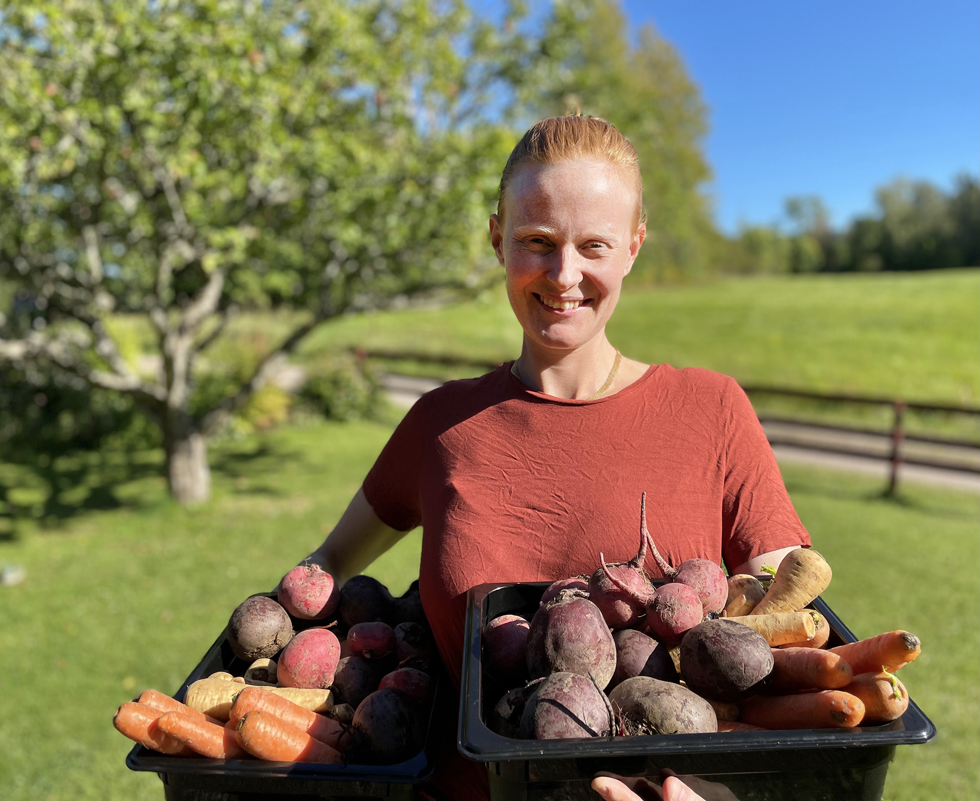 Kvinna visar upp tråg med olika rotfrukter.