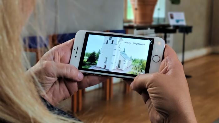 Över axeln ser vi någon titta på en bild av Stora Tuna kyrka i sin mobil