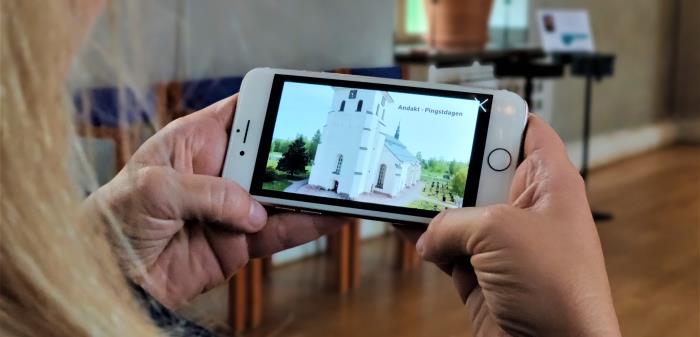 Över axeln ser vi någon titta på en bild av Stora Tuna kyrka i sin mobil