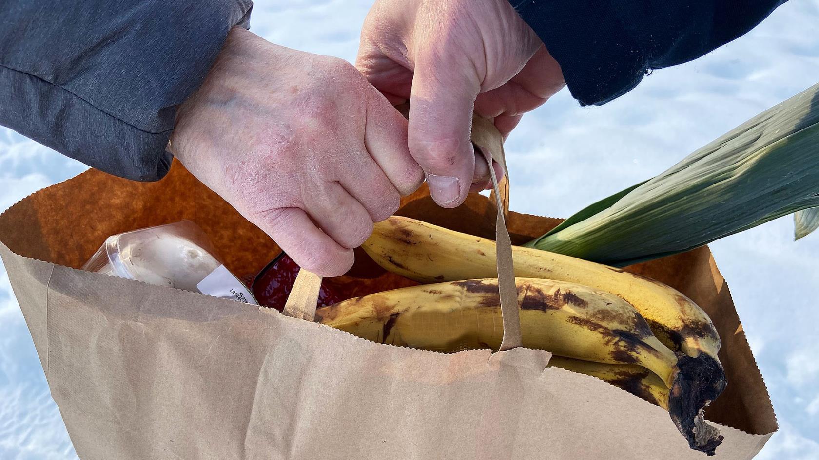 Överlämnade av en matkasse med bananer och purjolök som sticker upp.