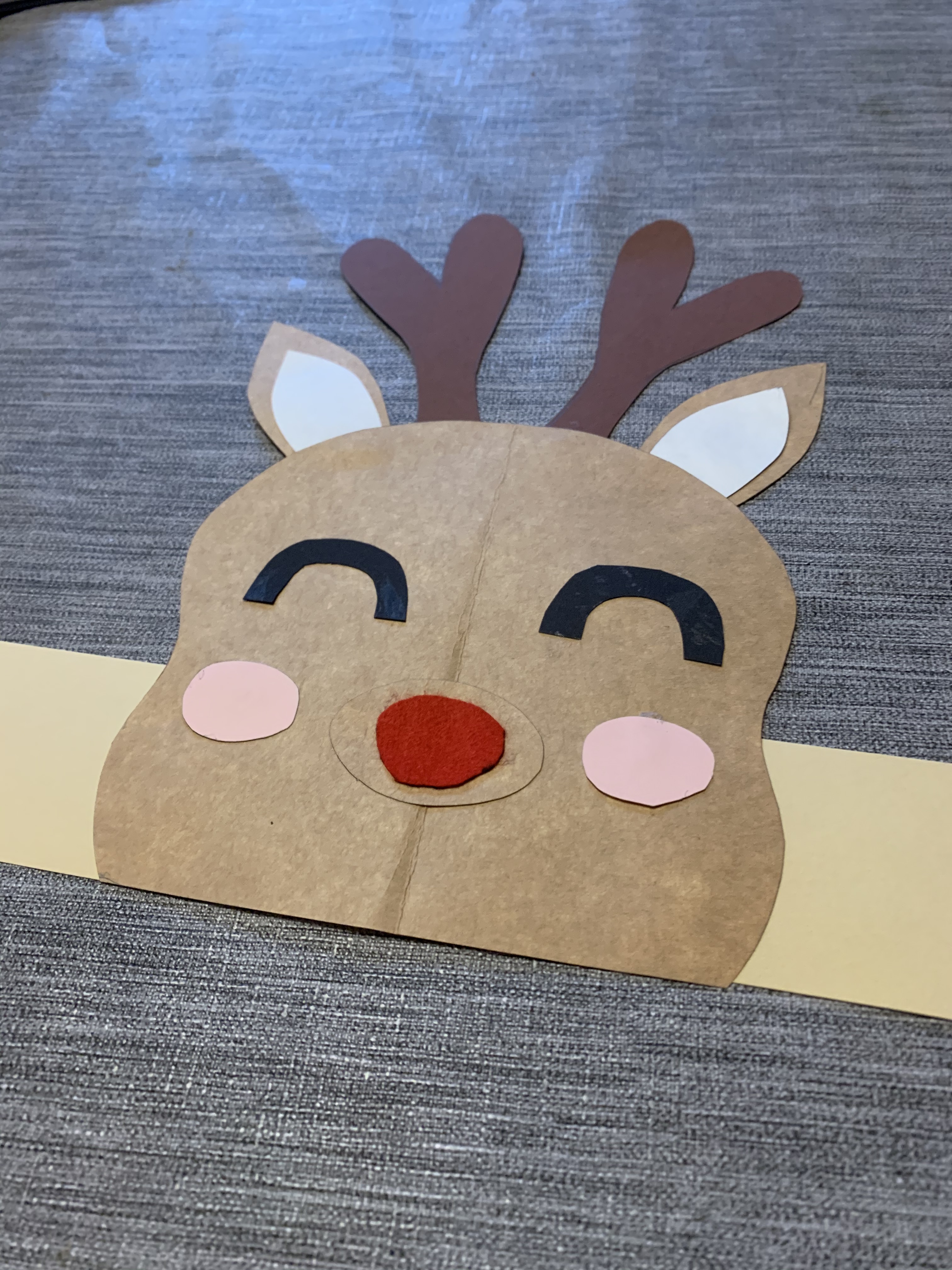 En ihoppysslad pappertiara i form av en ren, med horn, röd nos, rosa kinder, ljusbrunt huvud, öron och blundande ögon.
