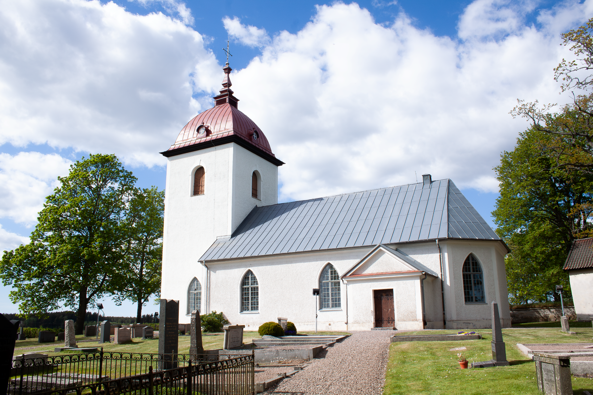 En vit kyrka med rött tak på tornet och grått tak på långhuset.