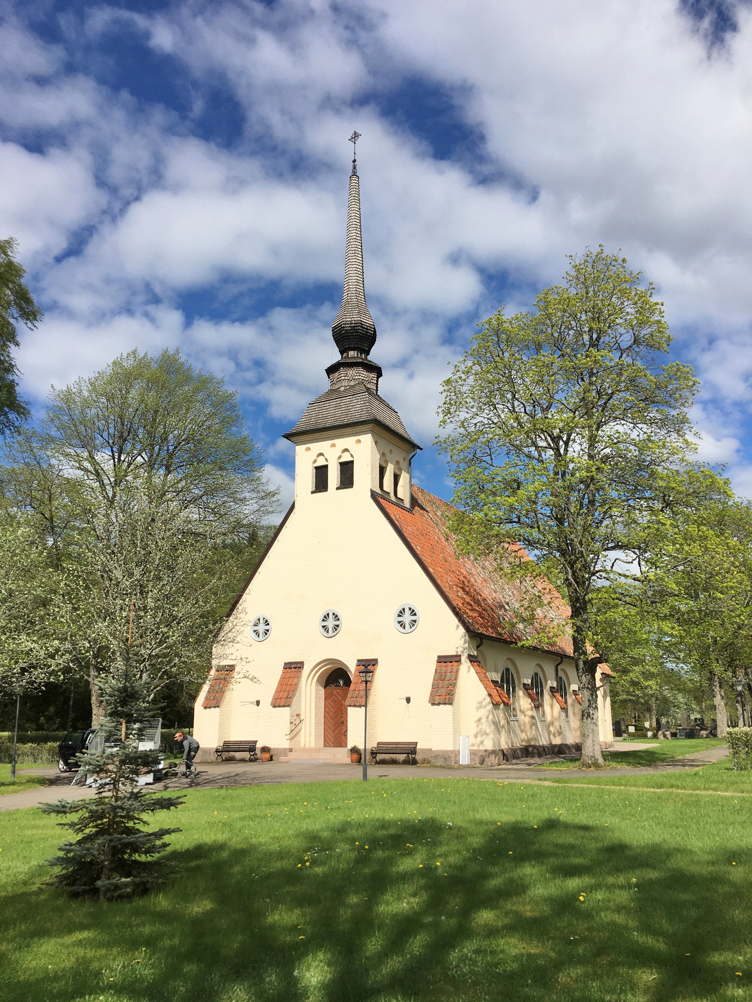 En kyrka bland grönt gräs och lummiga träd.