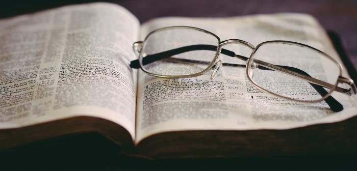 Bibel uppslagen med ett par glasögon ihopvikta ovanpå.