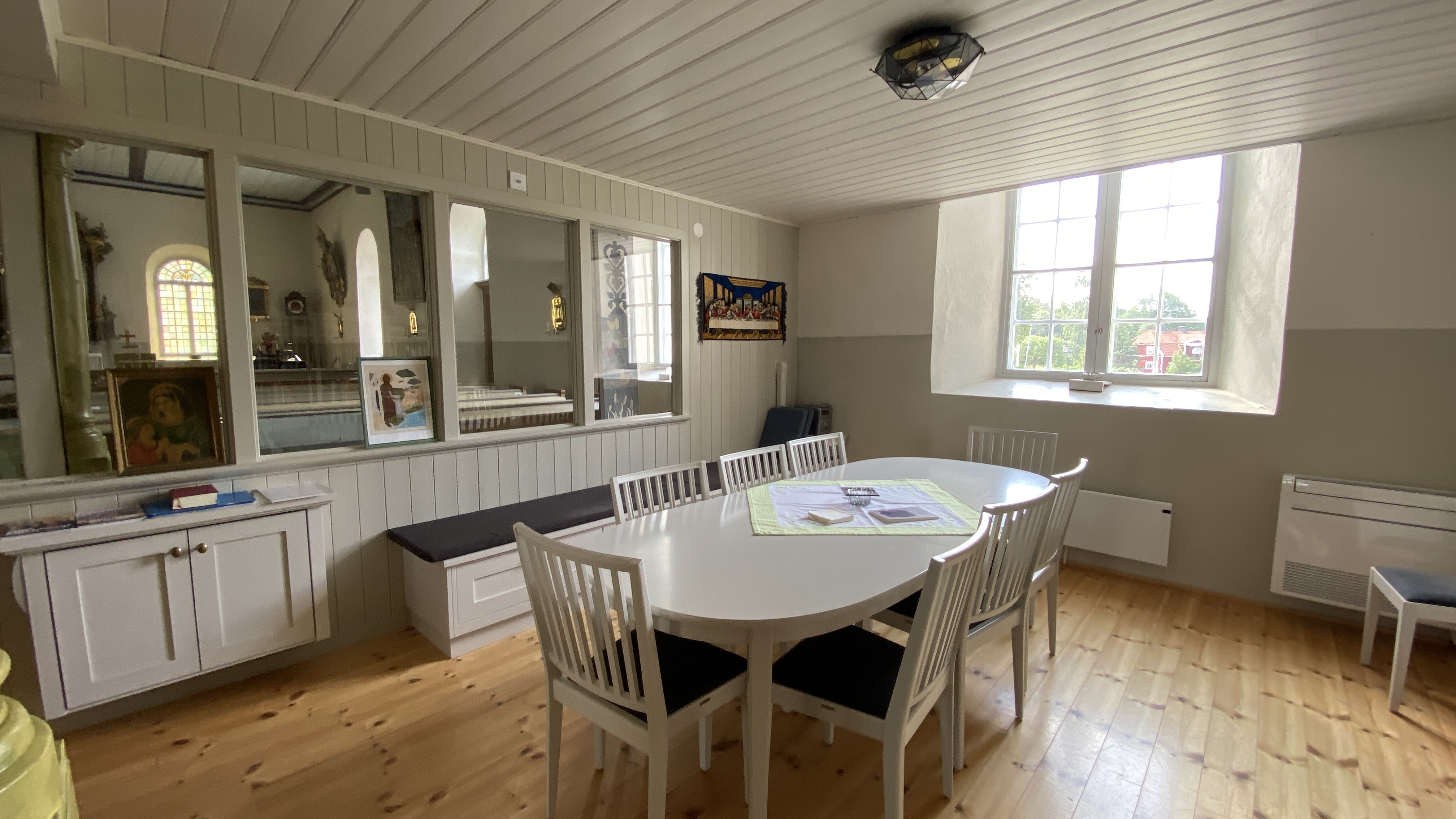 Ett vitt långbord framför ett fönster och bredvid några fönster som visar kyrkorummet. 