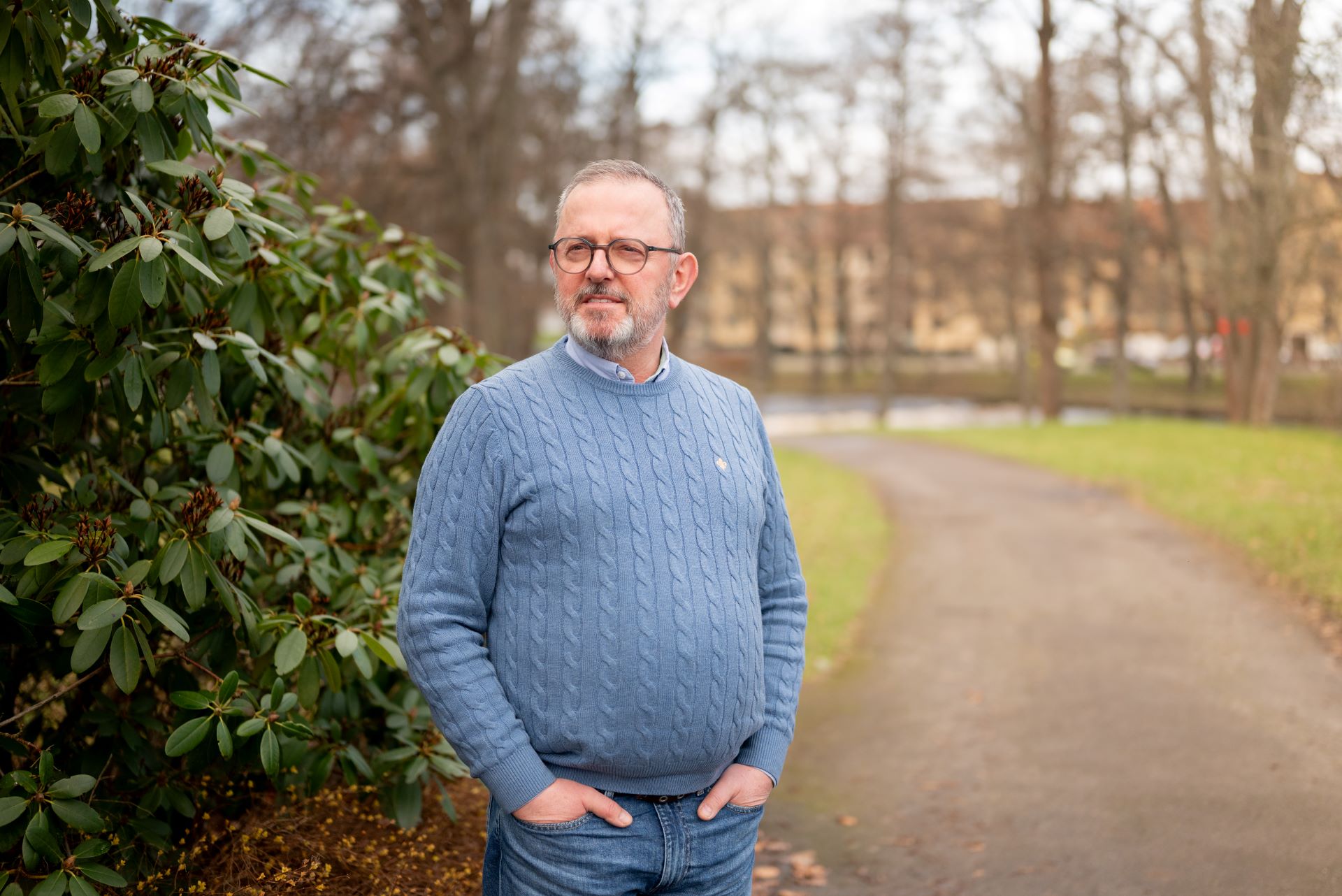 EN man står vid en grusväg och tittar upp. I bakgrunden syns en buske.