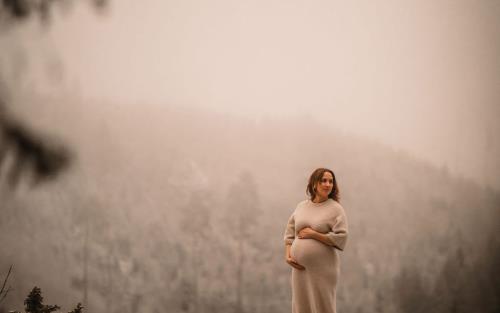 En gravid kvinna står barfota på en klippa och håller händerna på magen. 