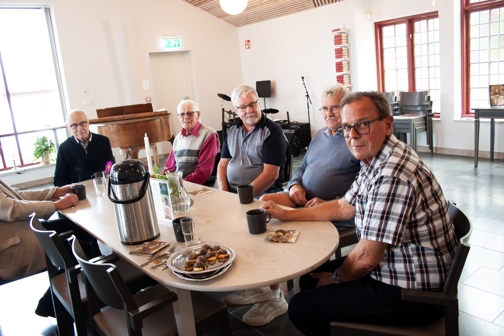 Fem äldre herrar sitter och fikar runt ett bord.