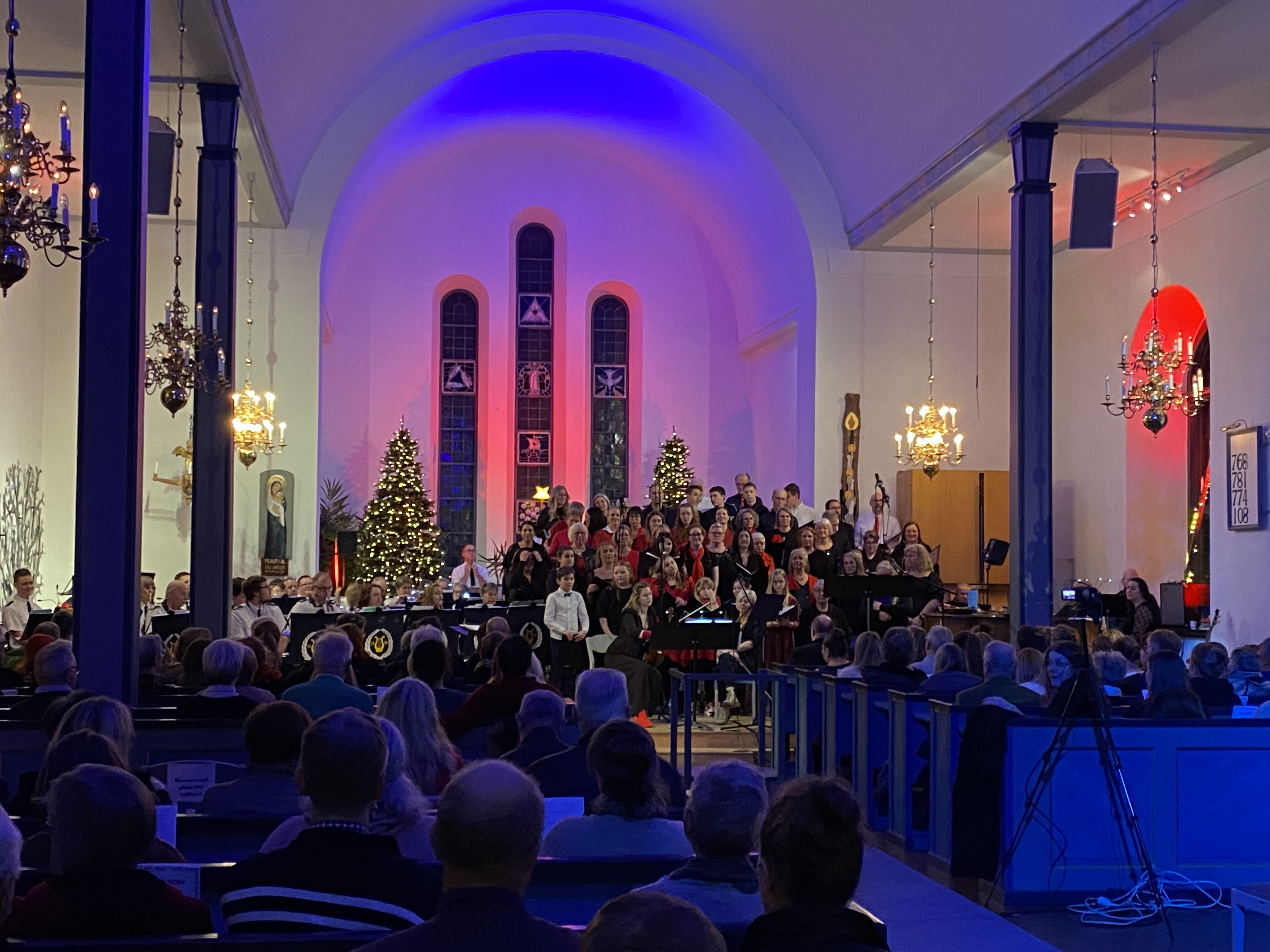 Koret i en kyrka är upplyst i blåa och röda toner, körer sjunger och en orkester spelar.