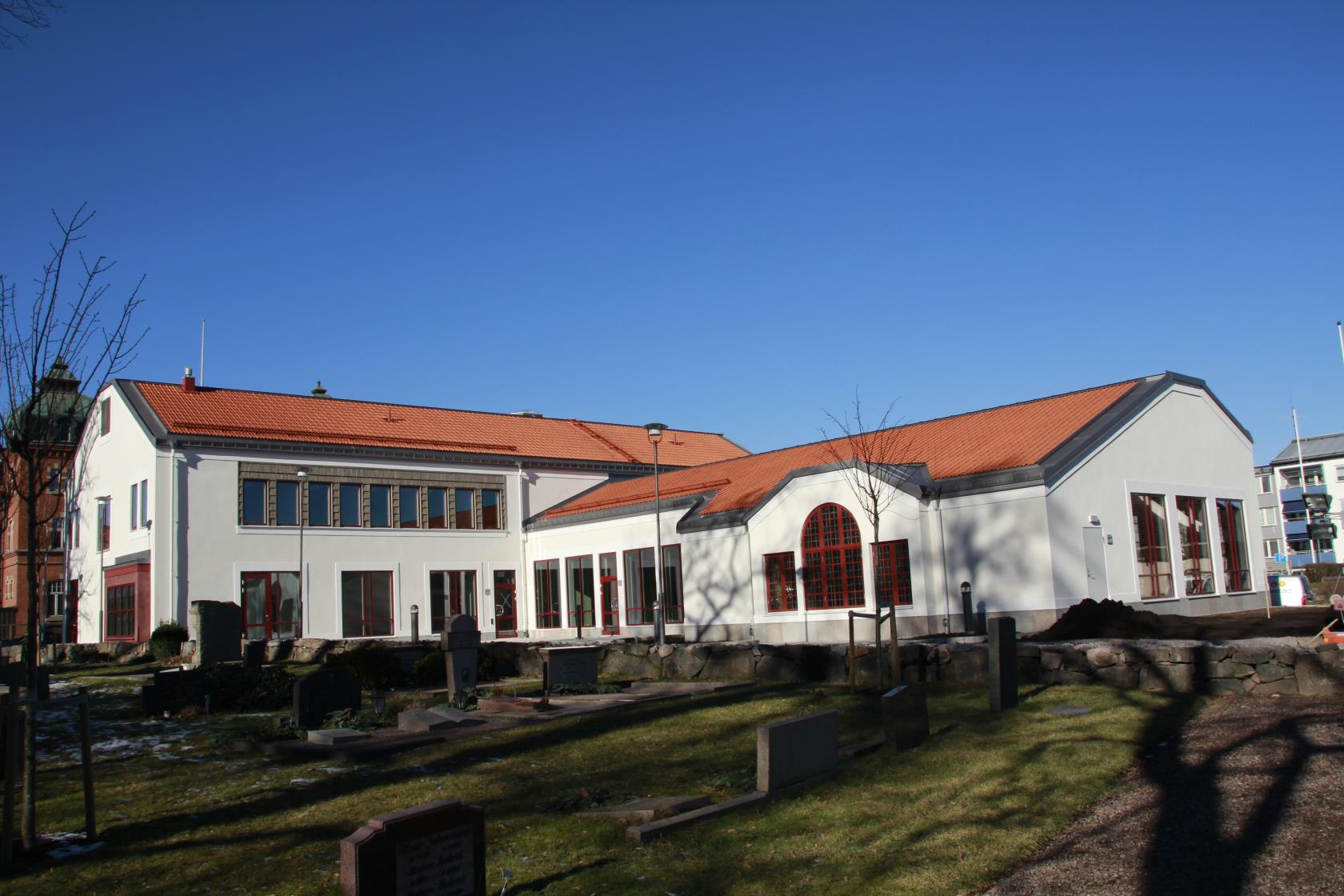 Kyrkans hus med kyrkogården och Tidaholms kyrka till vänster (utanför bilden), solen skiner och himlen är blå.
