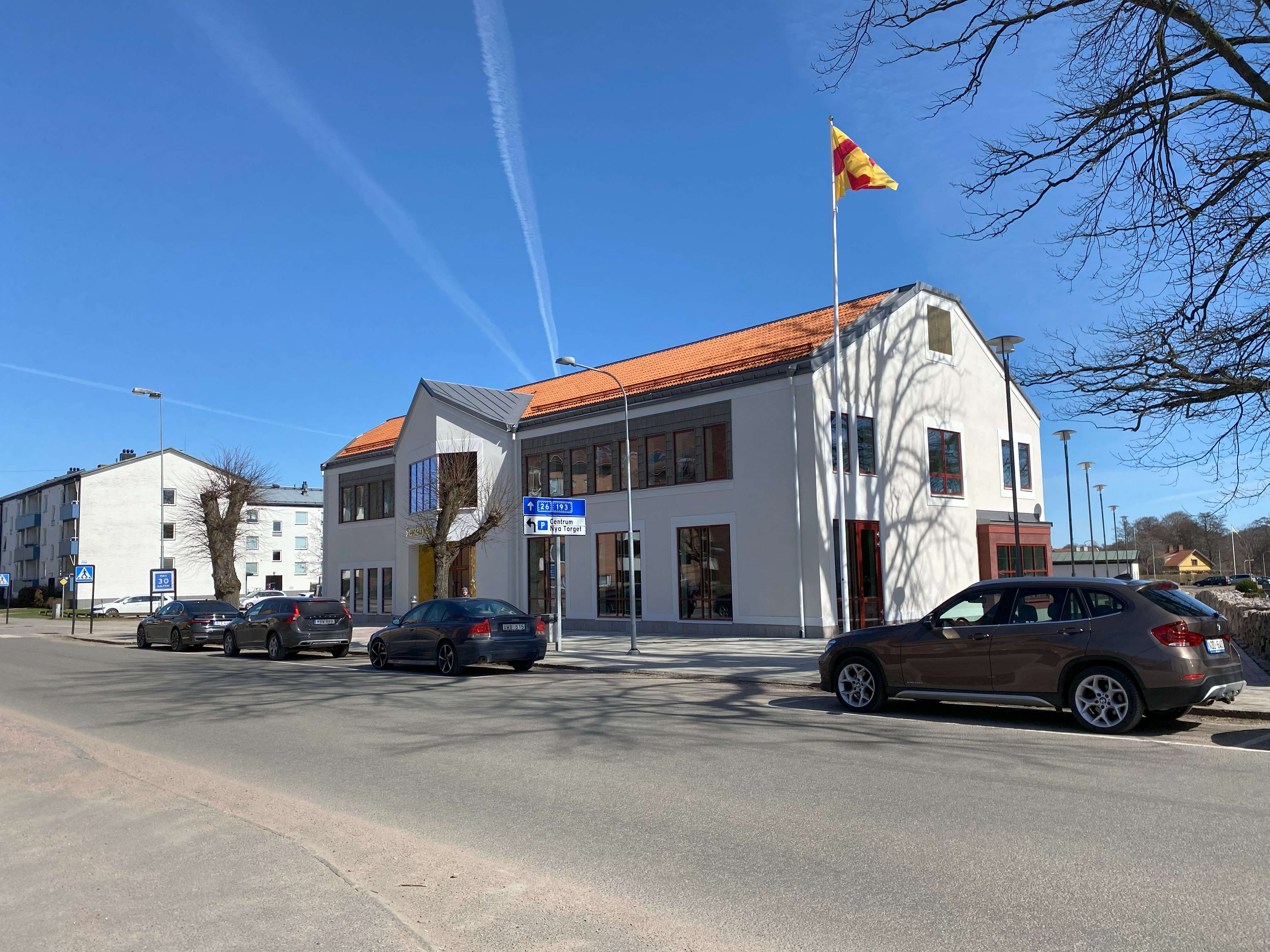 En bilväg som går förbi Kyrkans hus, där är också en flaggstång med Svenska kyrkans flagga samt några bilar vid sidan av vägen.