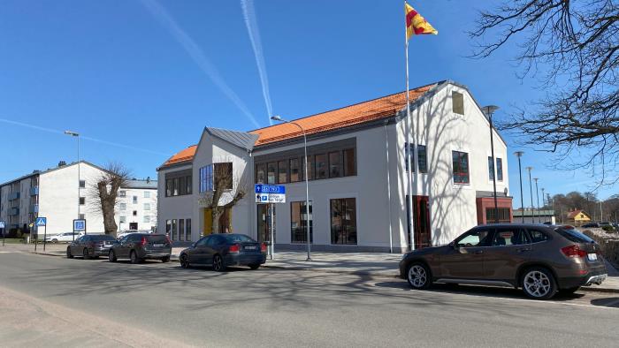 En bilväg som går förbi Kyrkans hus, där är också en flaggstång med Svenska kyrkans flagga samt några bilar vid sidan av vägen.