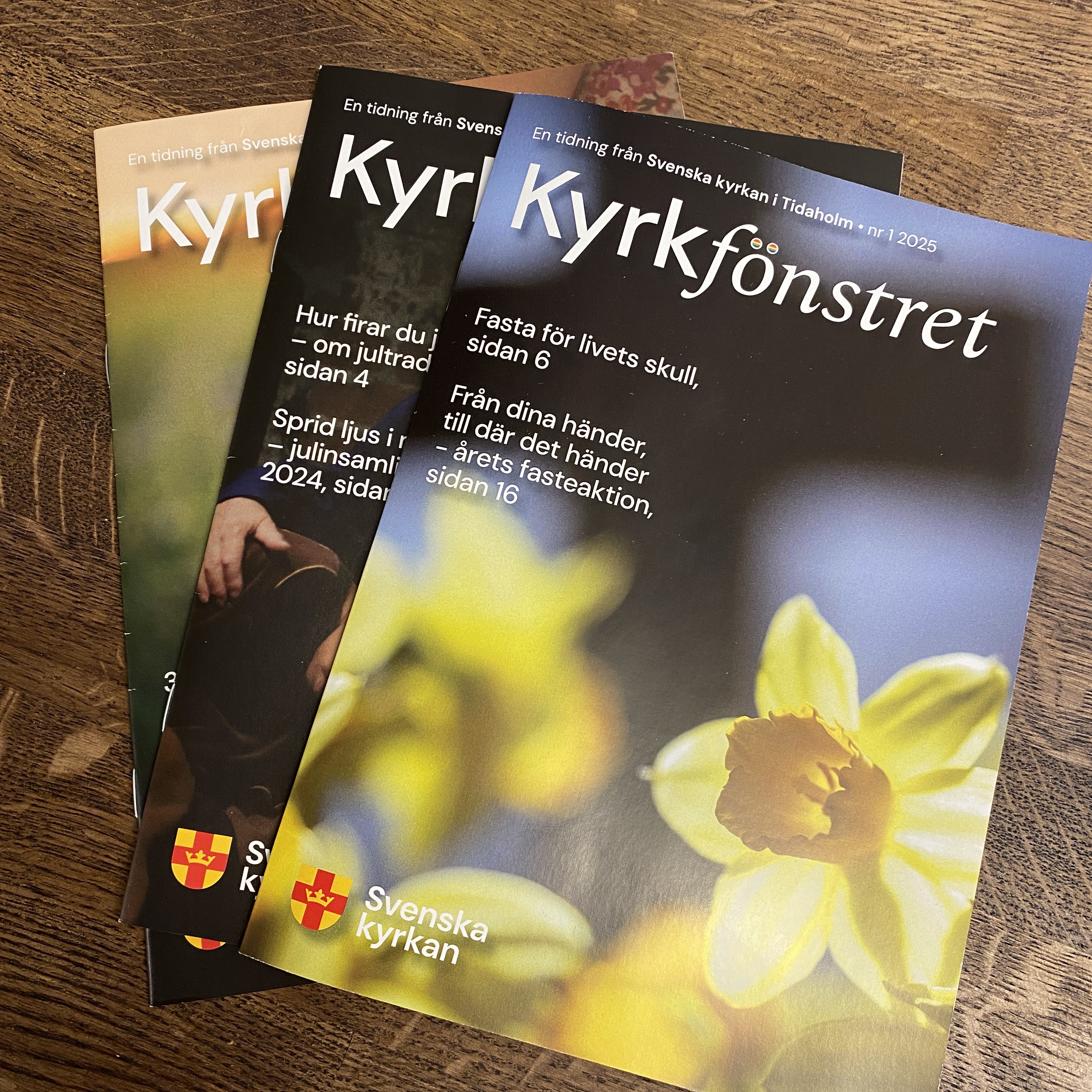 Tre olika nummer av församlingstidningen Kyrkfönstret i en hög.