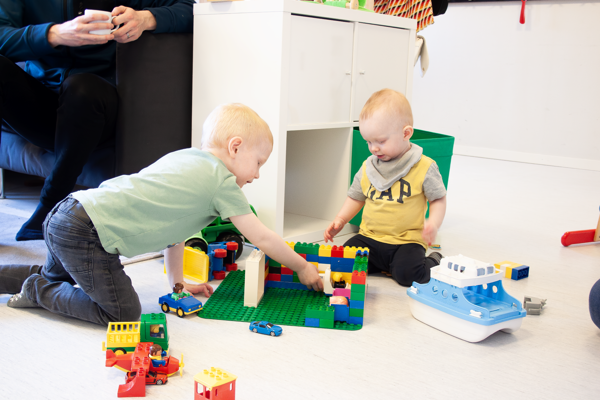 Två barn leker med byggklossar och leksaker, de är i olika åldrar.