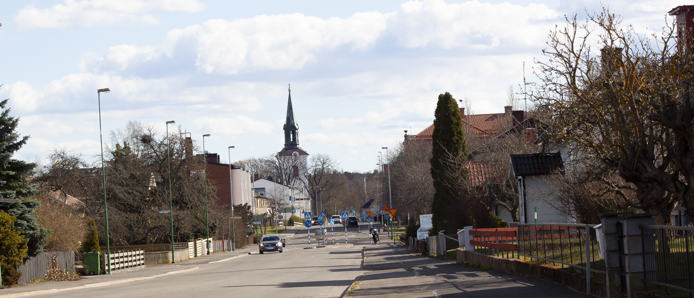 vy över Tidaholm med TIdaholms kyrka i centrum, bilar kör på vägen som omges av hus på vardera sida.