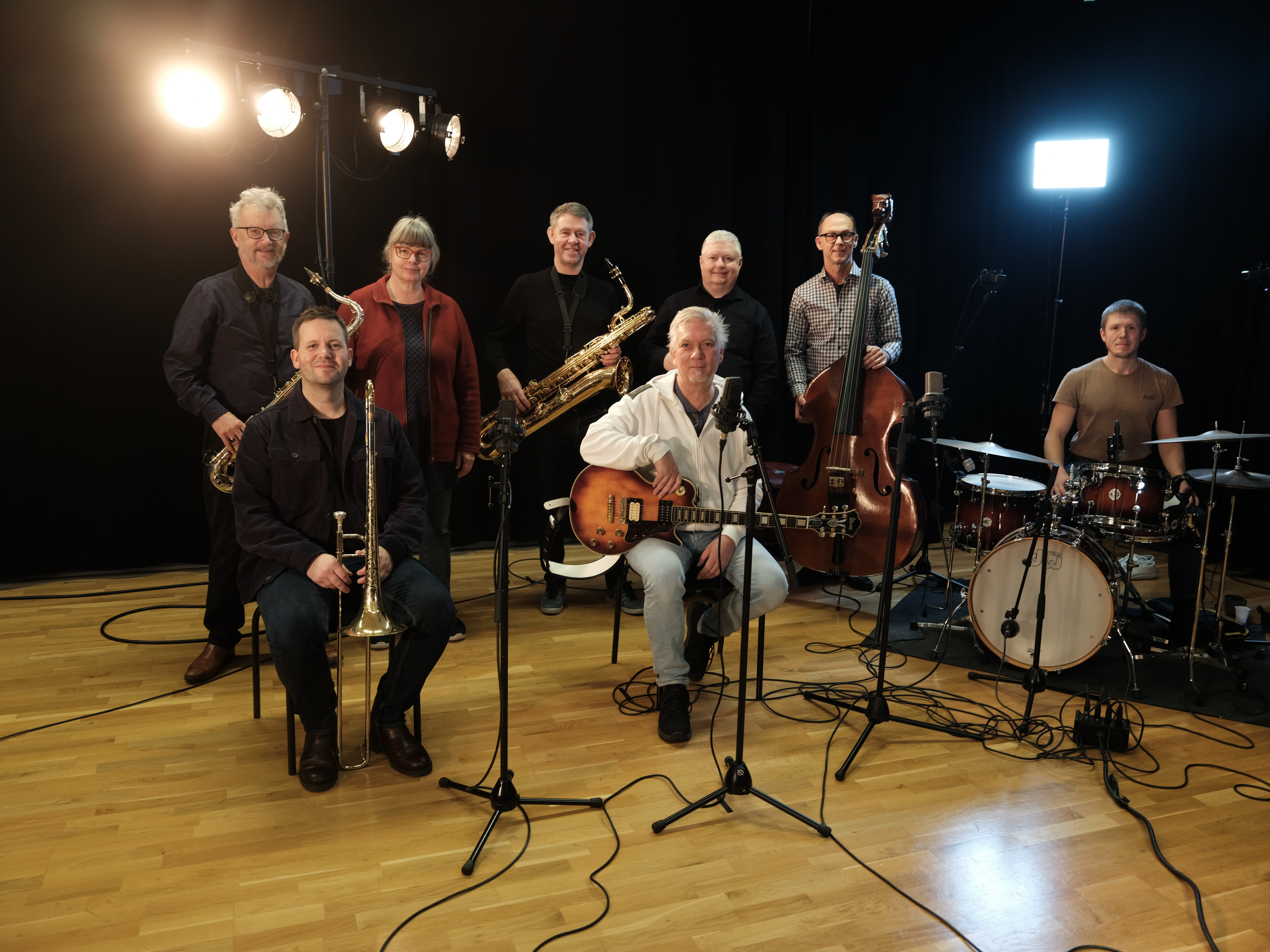 Åtta personer med instrument, några står och några sitter i en musiksal.