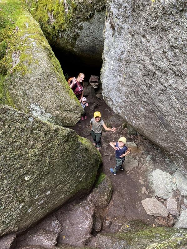 Tre personer står bland två klippblock och tittar upp.