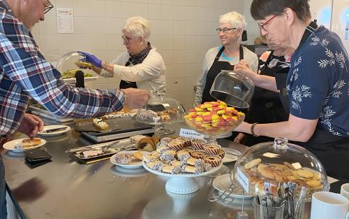 Volontärer i svarta förkläden med Svenska kyrkan Tidaholms logga på hjälper torgcafékunder.