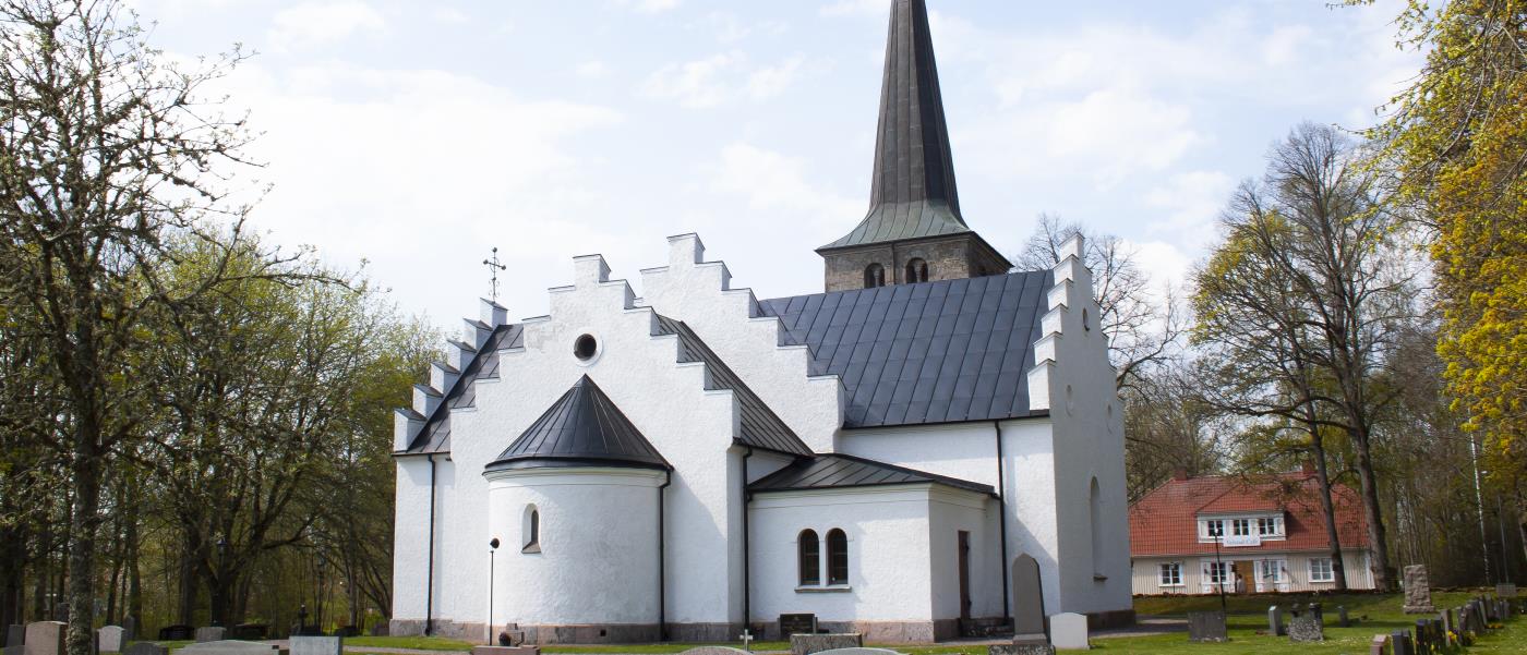 Valstads kyrka sett bakifrån, runt omkring är det gröna träd och grönt gräs på marken samt en mur som omger kyrkan.