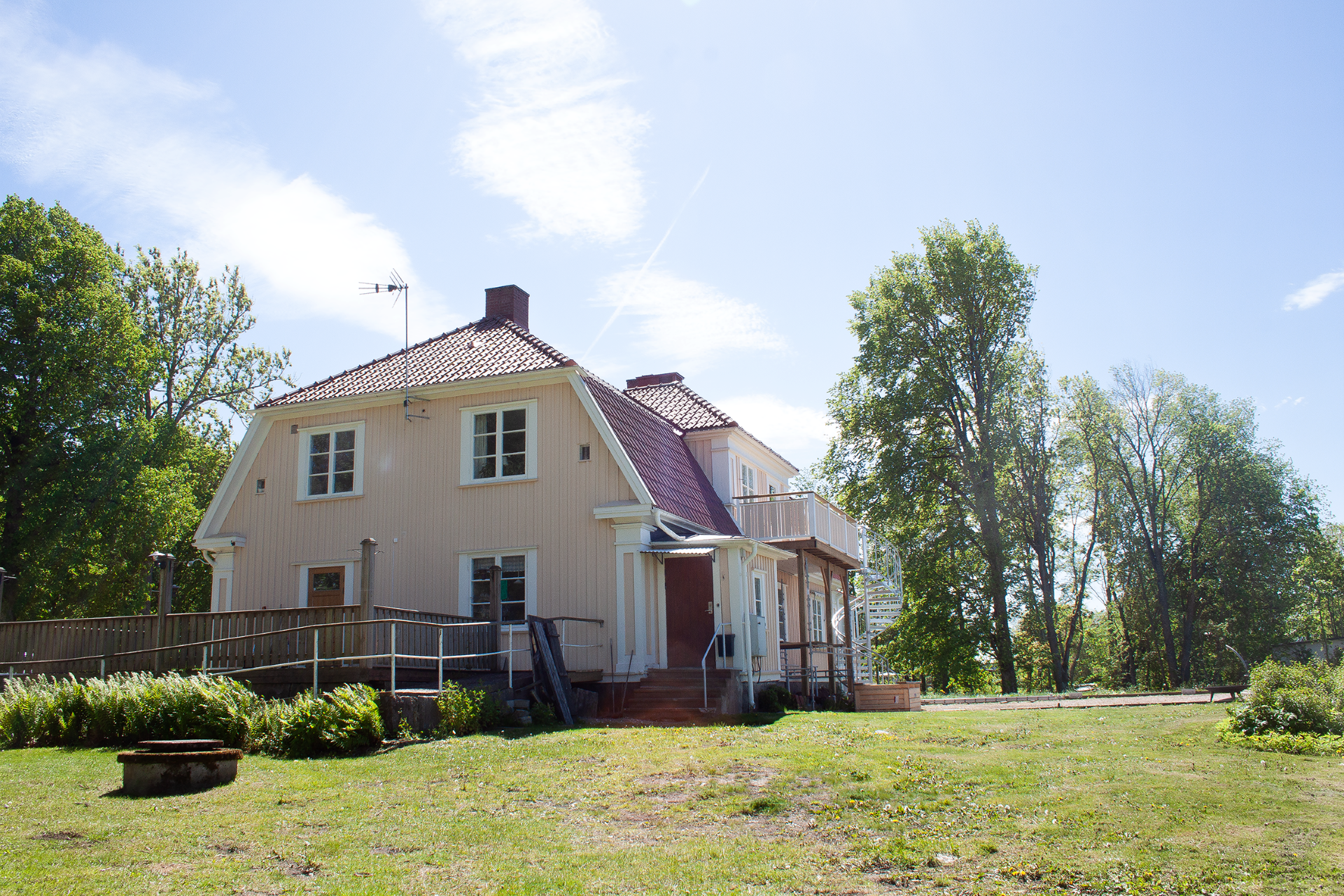 Ett beigemålat hus omgiven av grönska.