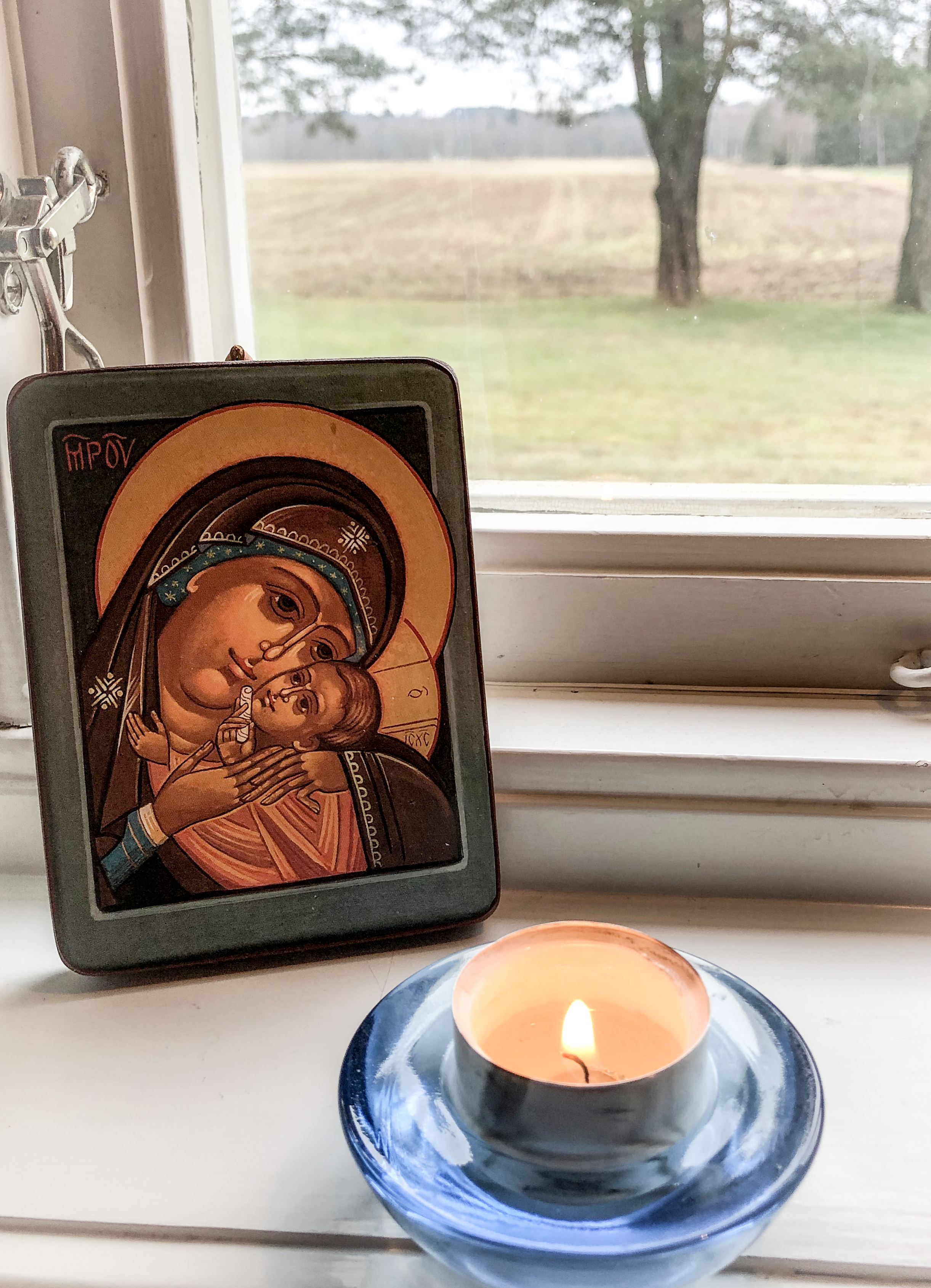 Ett värmeljus i ljushållare och en ikonbild ståendes i ett ljust fönster.