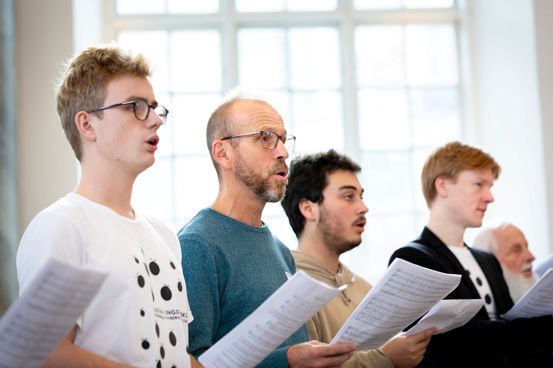 Fyra män i olika åldrar håller noter och sjunger tillsammans i en kyrka