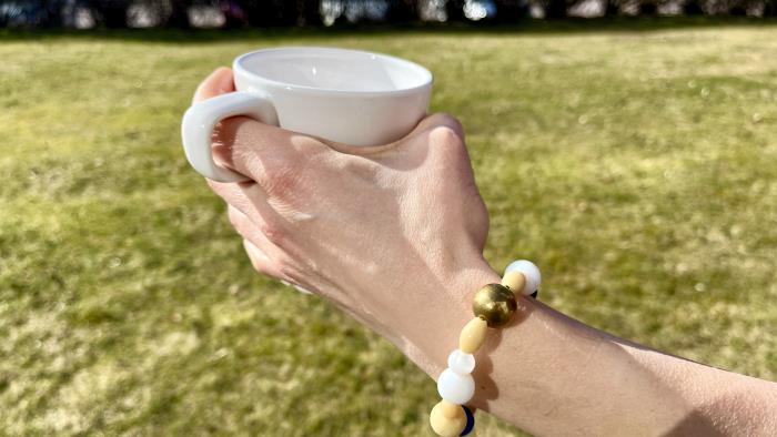 Hand håller kaffemugg i vårsolen med frälsarkrans runt armen