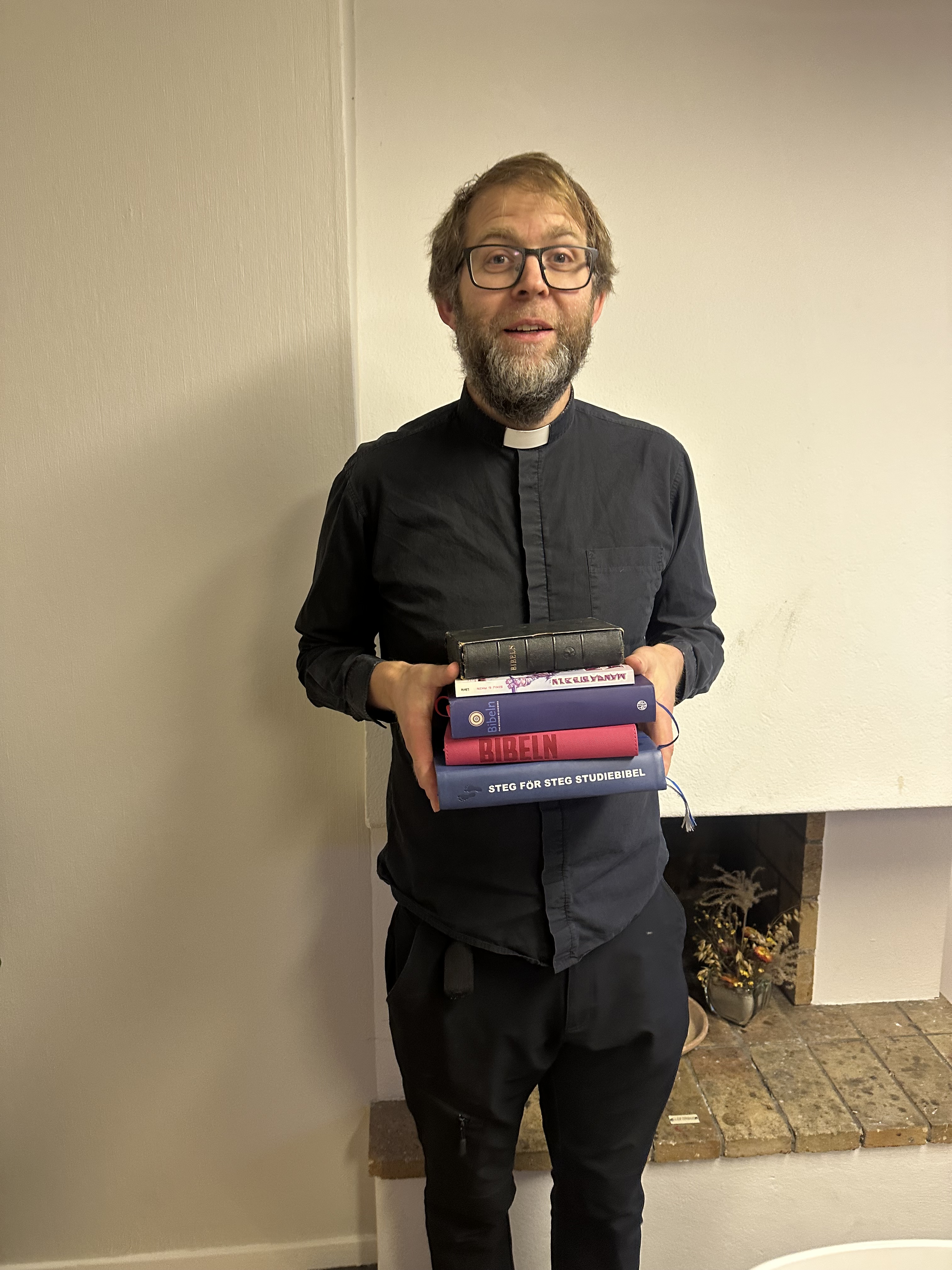 Man med glasögon står och håller i 5 stycken biblar