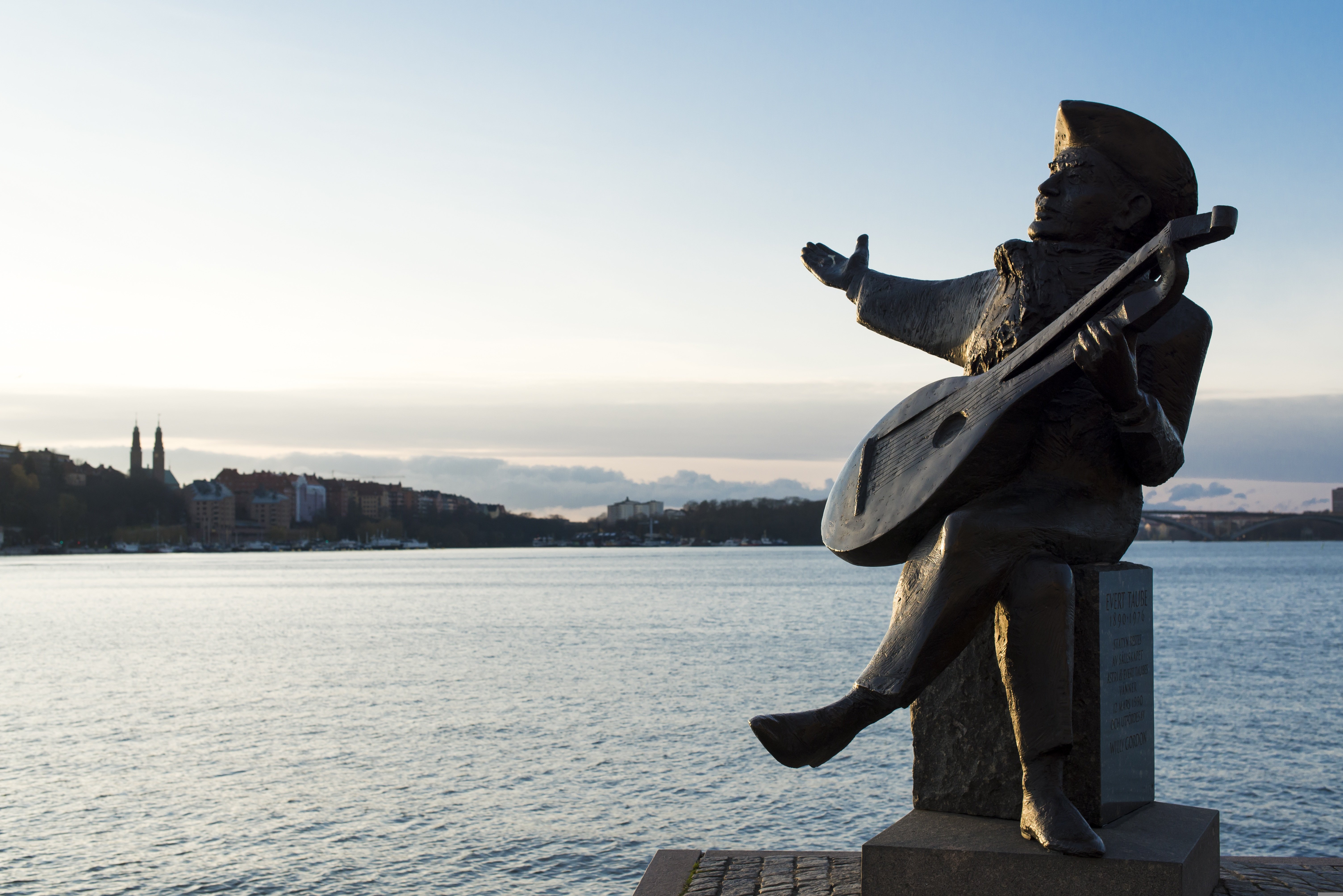 Evert Taube sitter med utsträckt hand vid havet.
