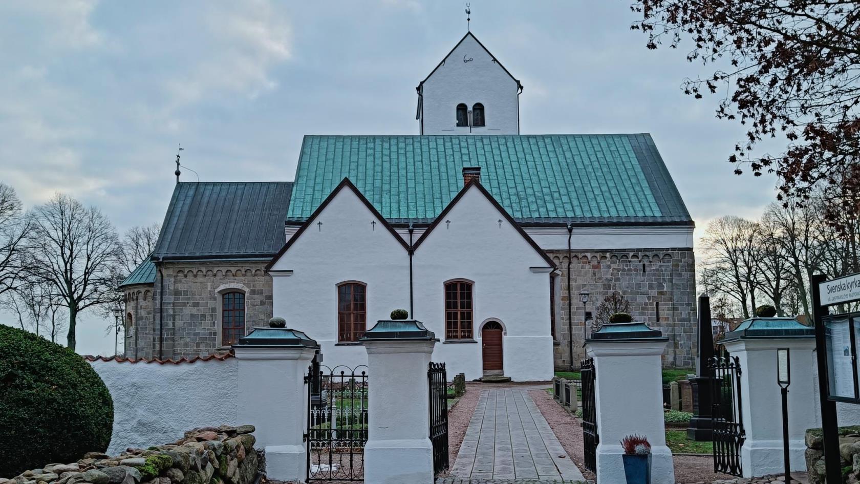 Ingång genom kyrkmur med vitkalkad kyrka i bakgrunden.