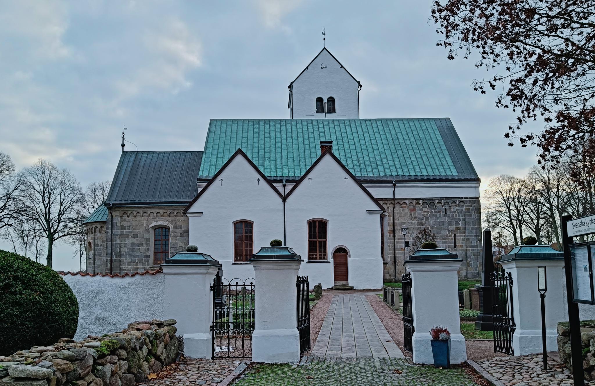 Ingång genom kyrkmur med vitkalkad kyrka i bakgrunden.