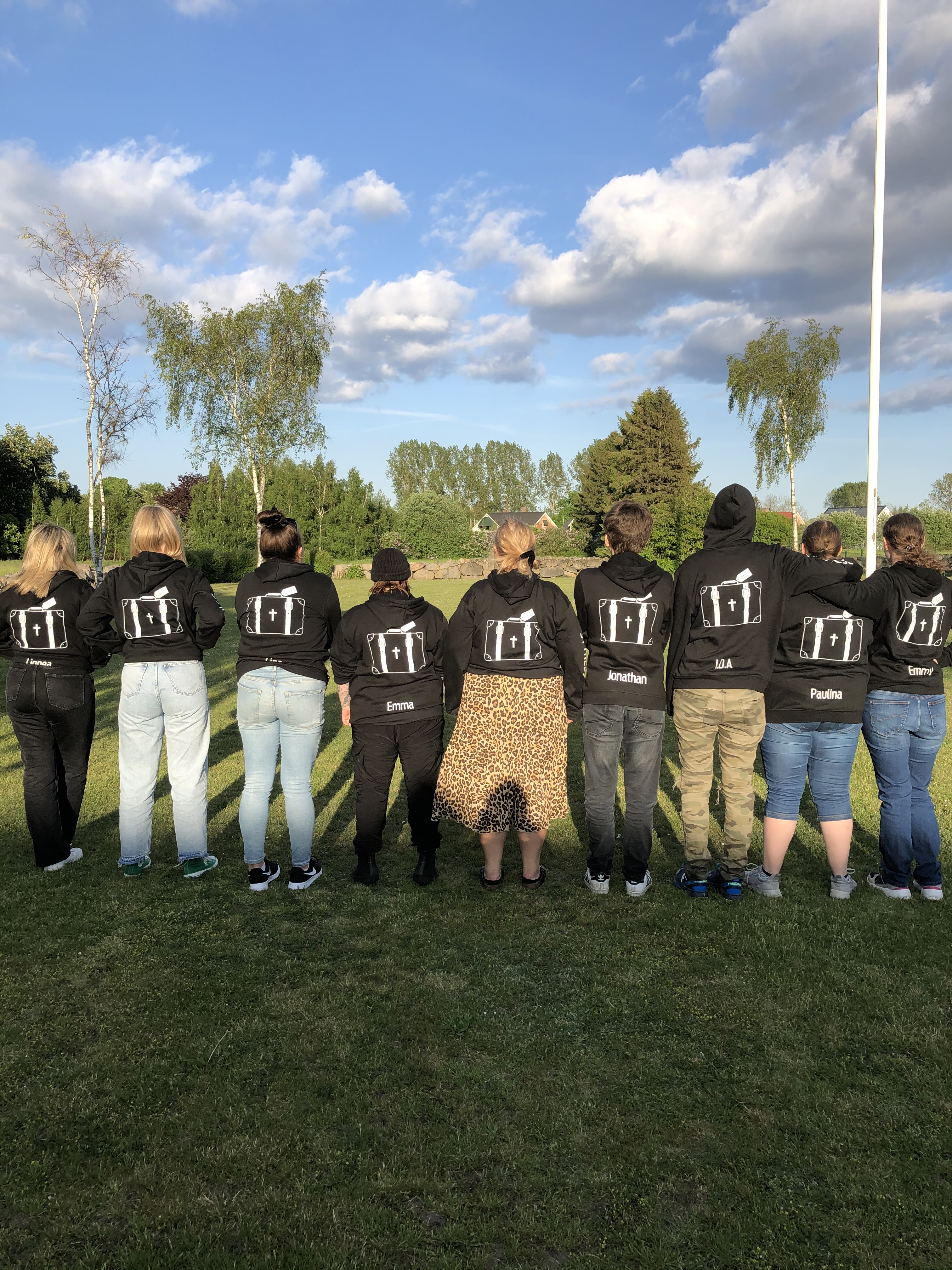 Ungdomar uppställda på rad med ryggen emot iklädda svart munktröja med "Väskans" logga på.