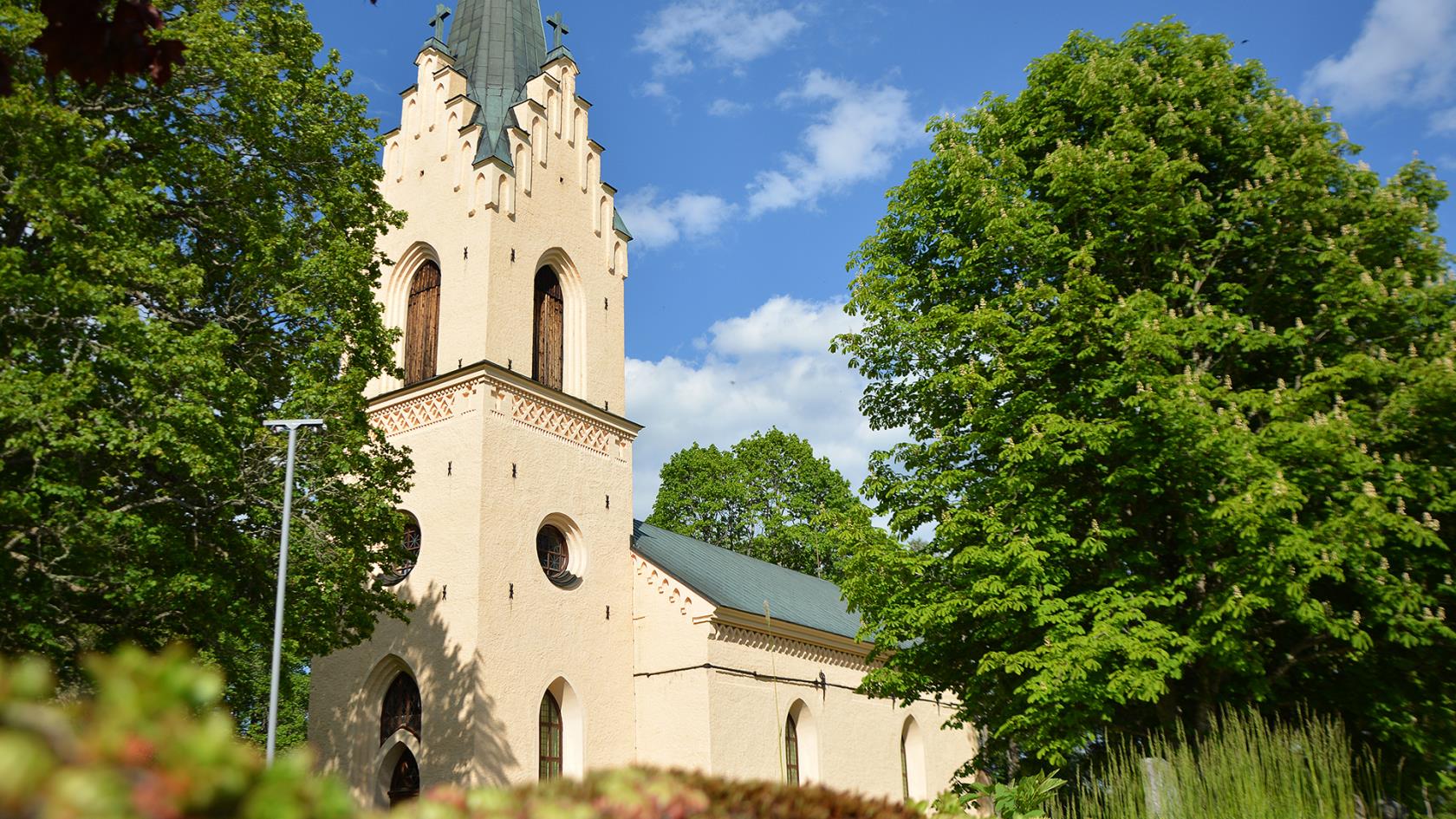 Enåkers kyrka mellan grönskande träd.