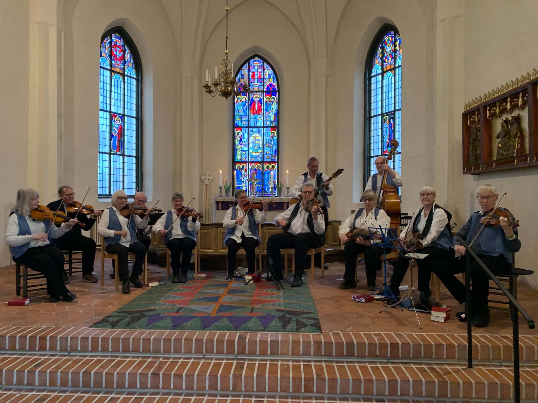 Spelmän i vita skjortor och blå västar spelar i en kyrka.