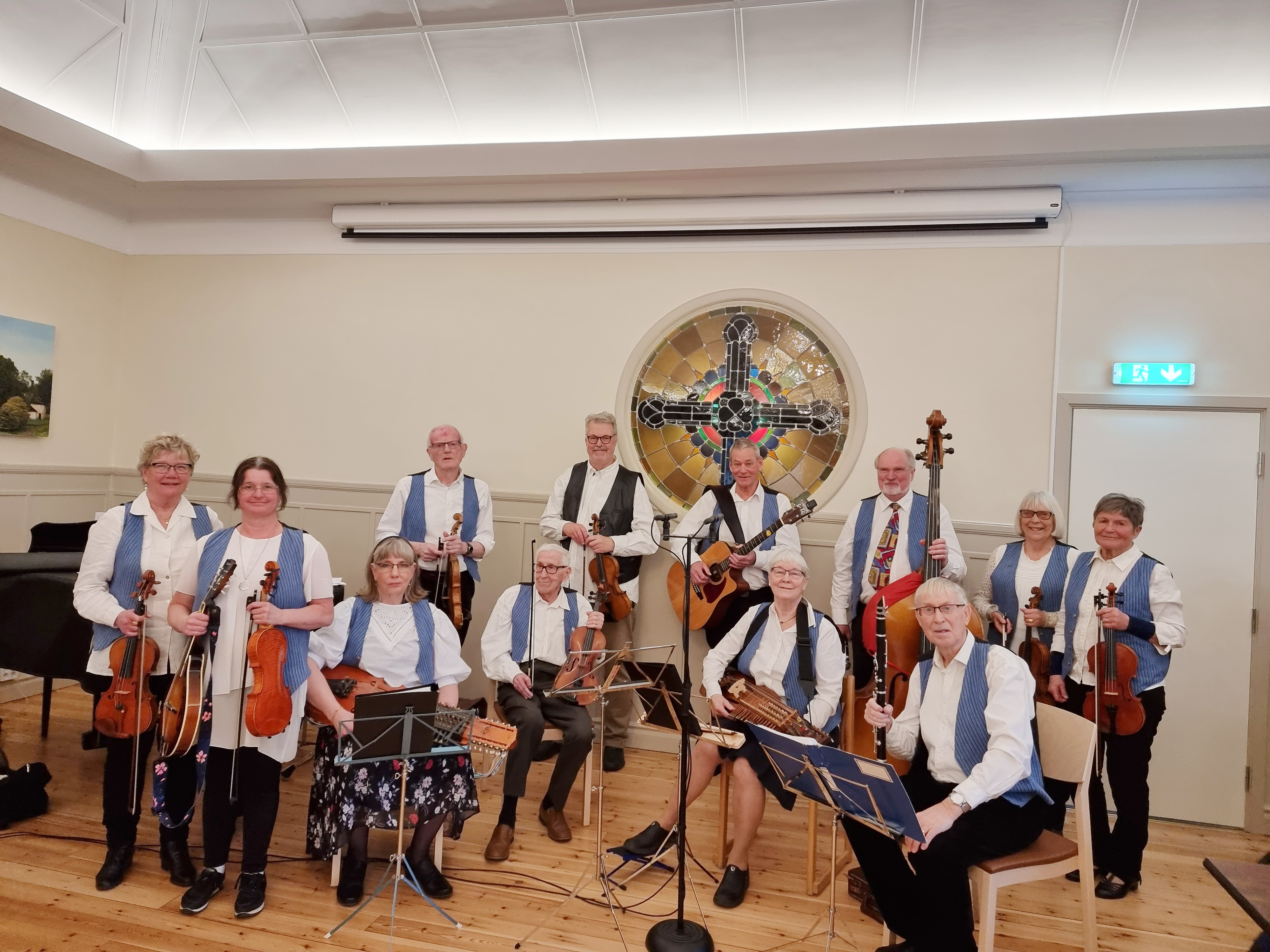 Ett gäng män och kvinnor i vita skjortor och blå västar med olika musikinstrument.