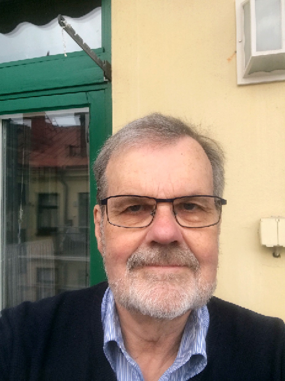 Porträtt av leende man med glasögon och grånande skägg.